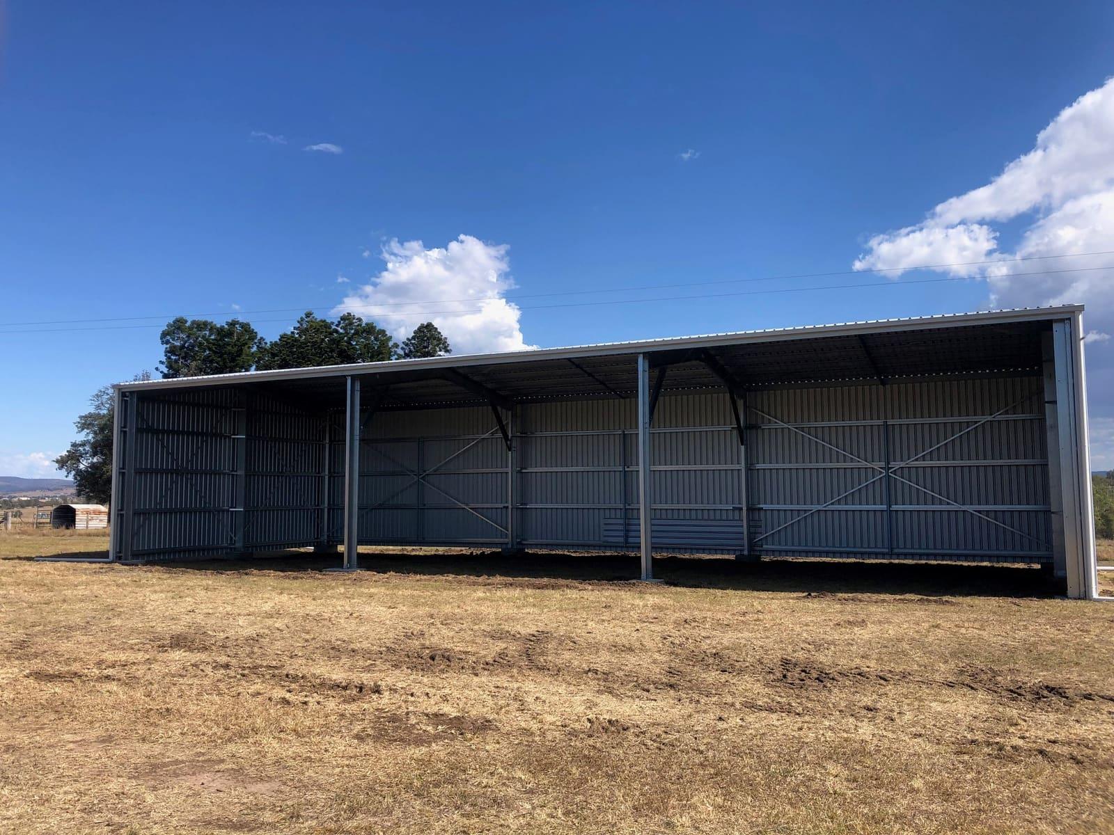 Open-front four-bay farm hay shed on a dry paddock under blue sky
