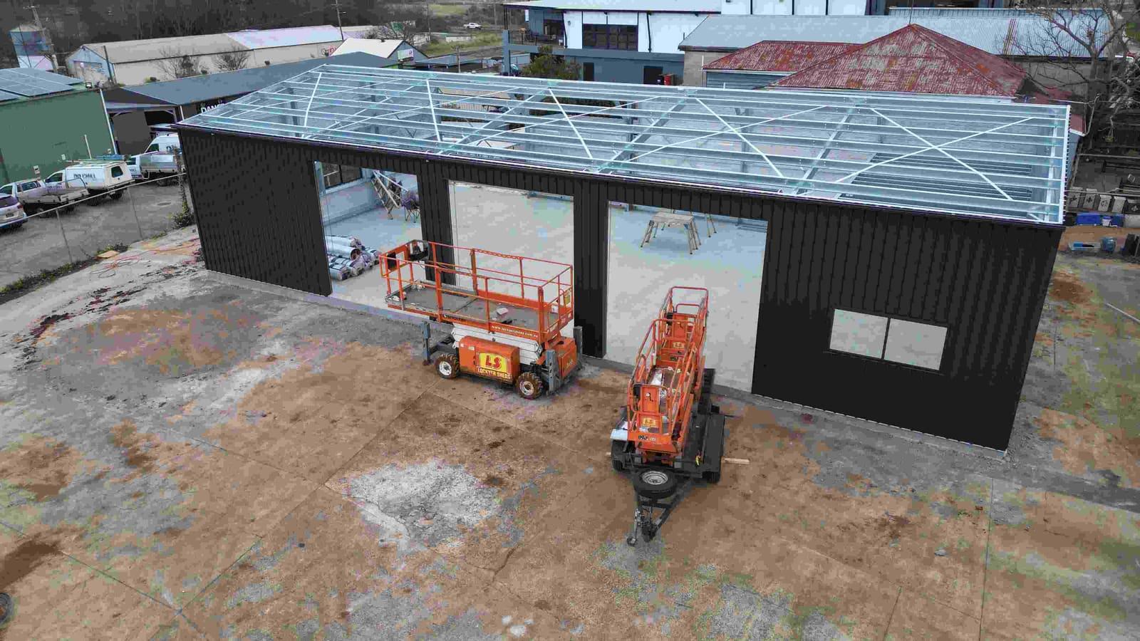 Aerial view of a dark steel industrial shed under construction with two Lockyer Sheds scissor lifts
