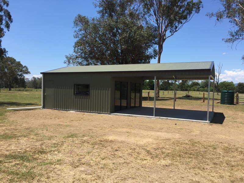 Olive-green shed with a side awning under large gum trees