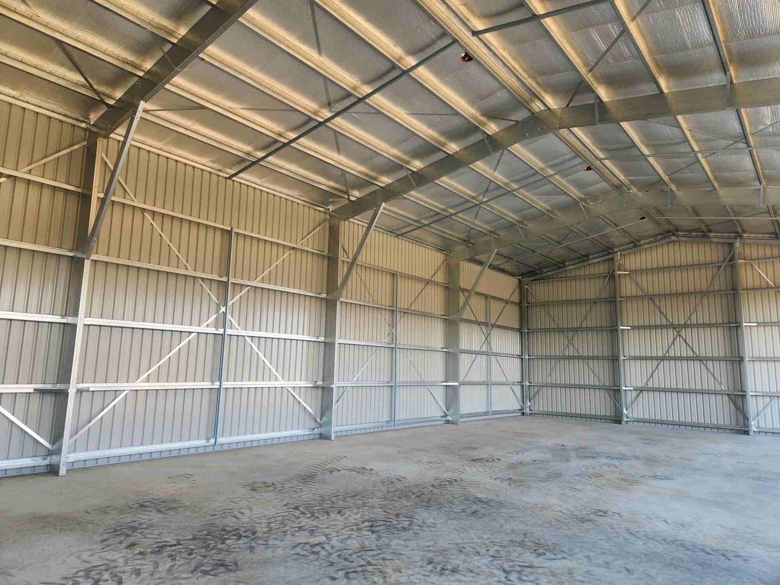 Inside a finished clear-span steel shed showing galvanised portal frames and cross bracing above a concrete slab